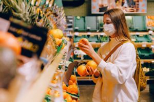 Masked woman picking oranges in supermarket